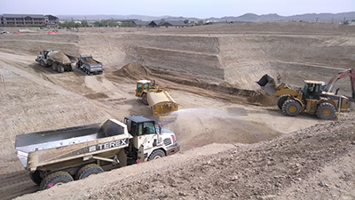 Excavator and haul trucks working a large earthwork cut